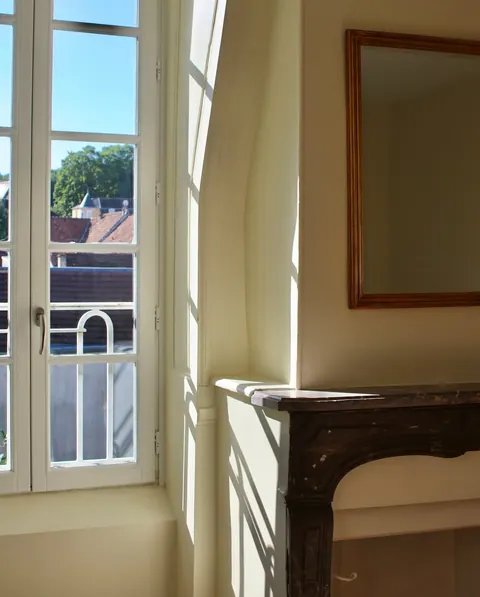 Chambre baignée de lumière, fenêtre ouverte sur les toits d'Écouen