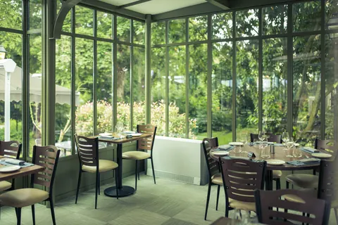 Tables dressées sous la verrière, la végétation du parc derrière les vitres